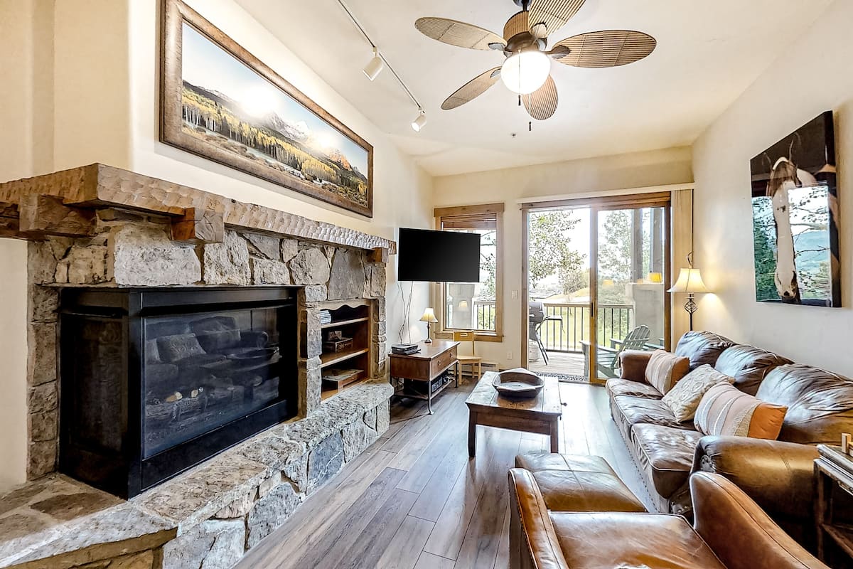 Una sala de estar con chimenea de piedra, sofá de cuero y televisor.