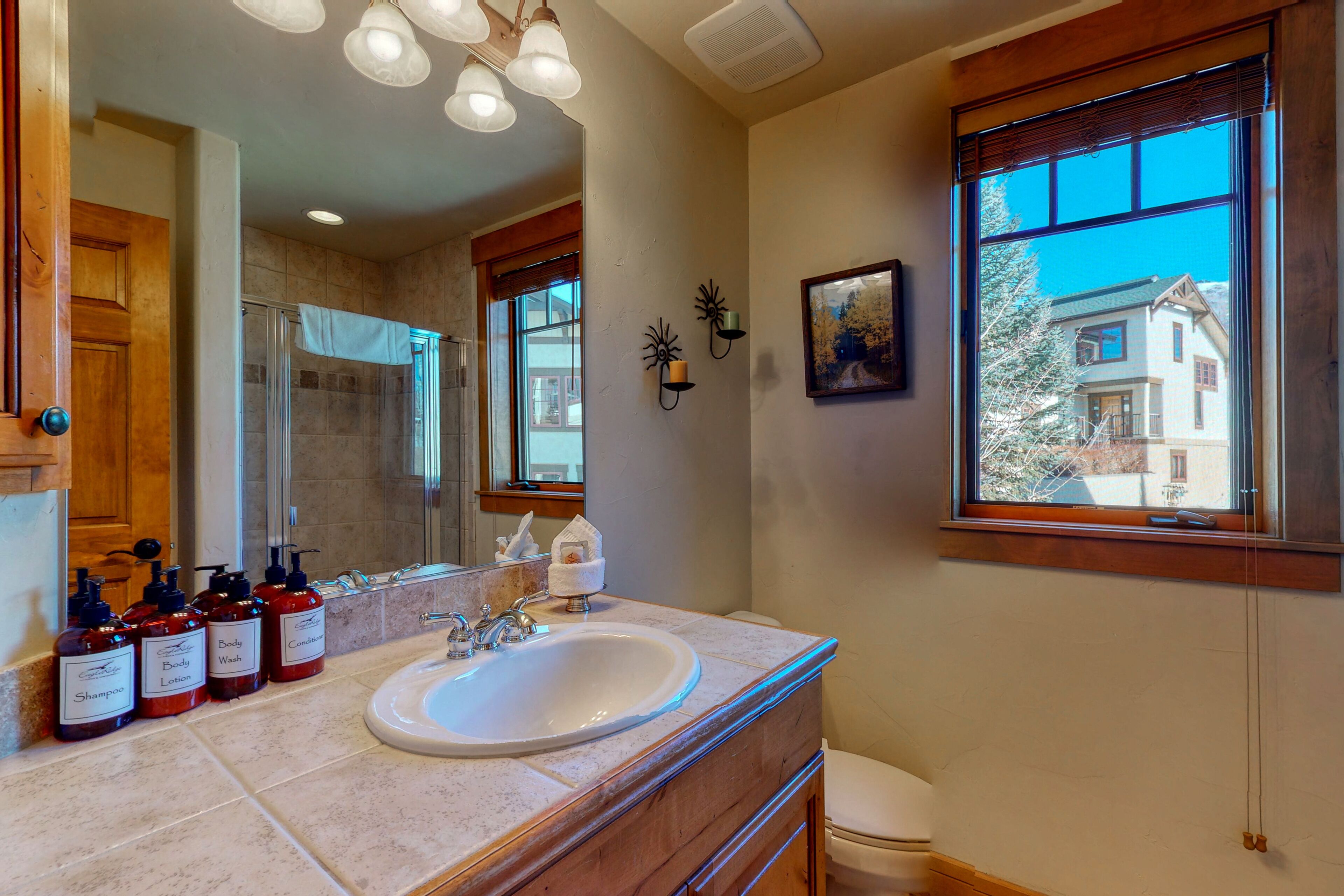 Un baño con un lavamanos grande, tocador de madera y una ventana con vista a una casa.
