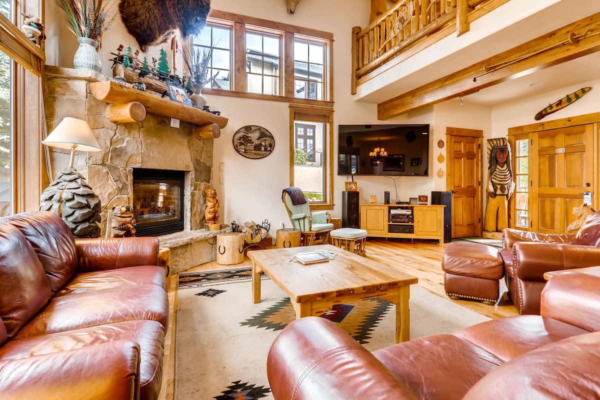 Un salón espacioso con sofás de cuero, una chimenea de piedra, vigas de madera y una televisión.