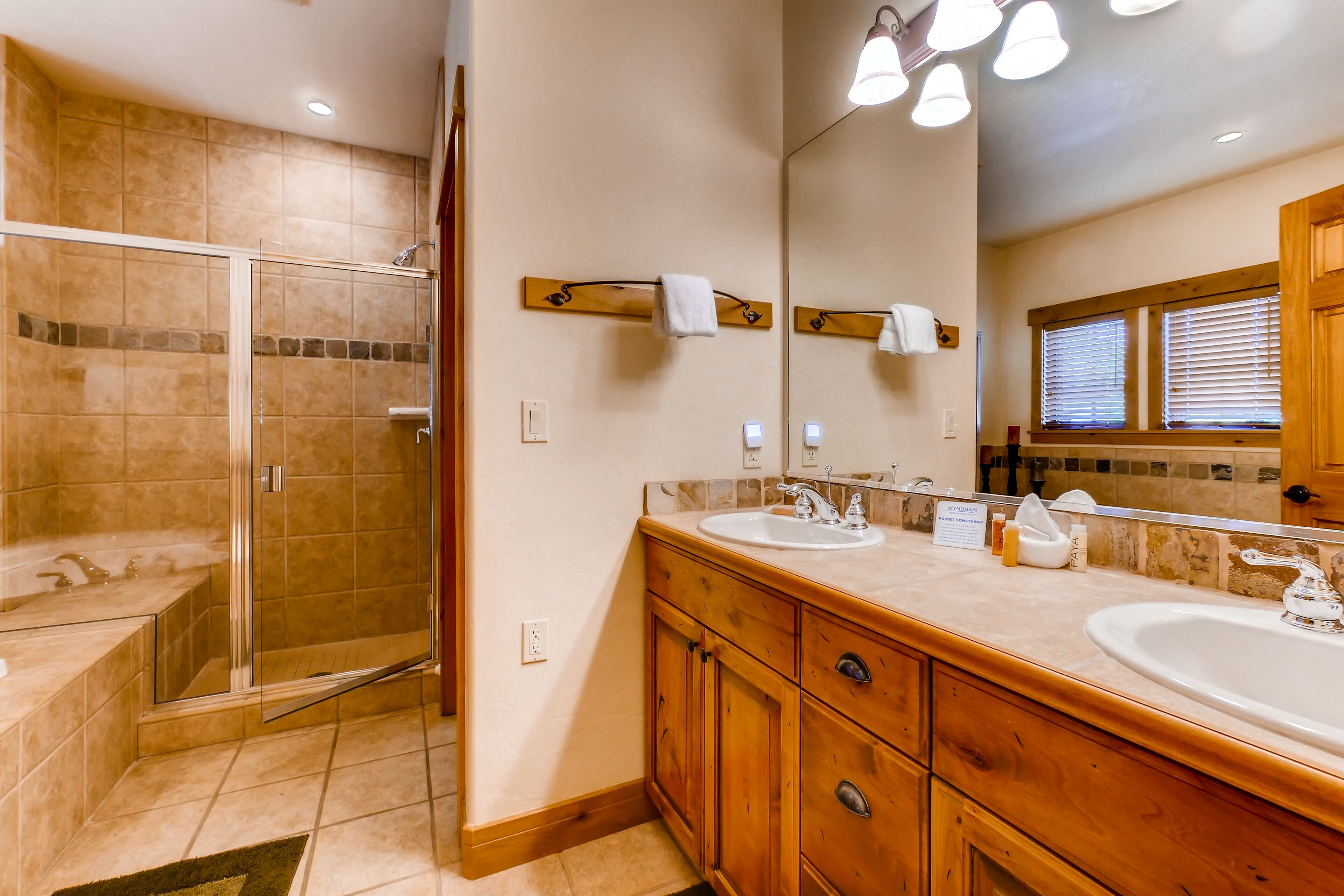 Un bagno con doccia vetrata, mobile contenitore in legno con doppio lavabo e uno specchio grande.