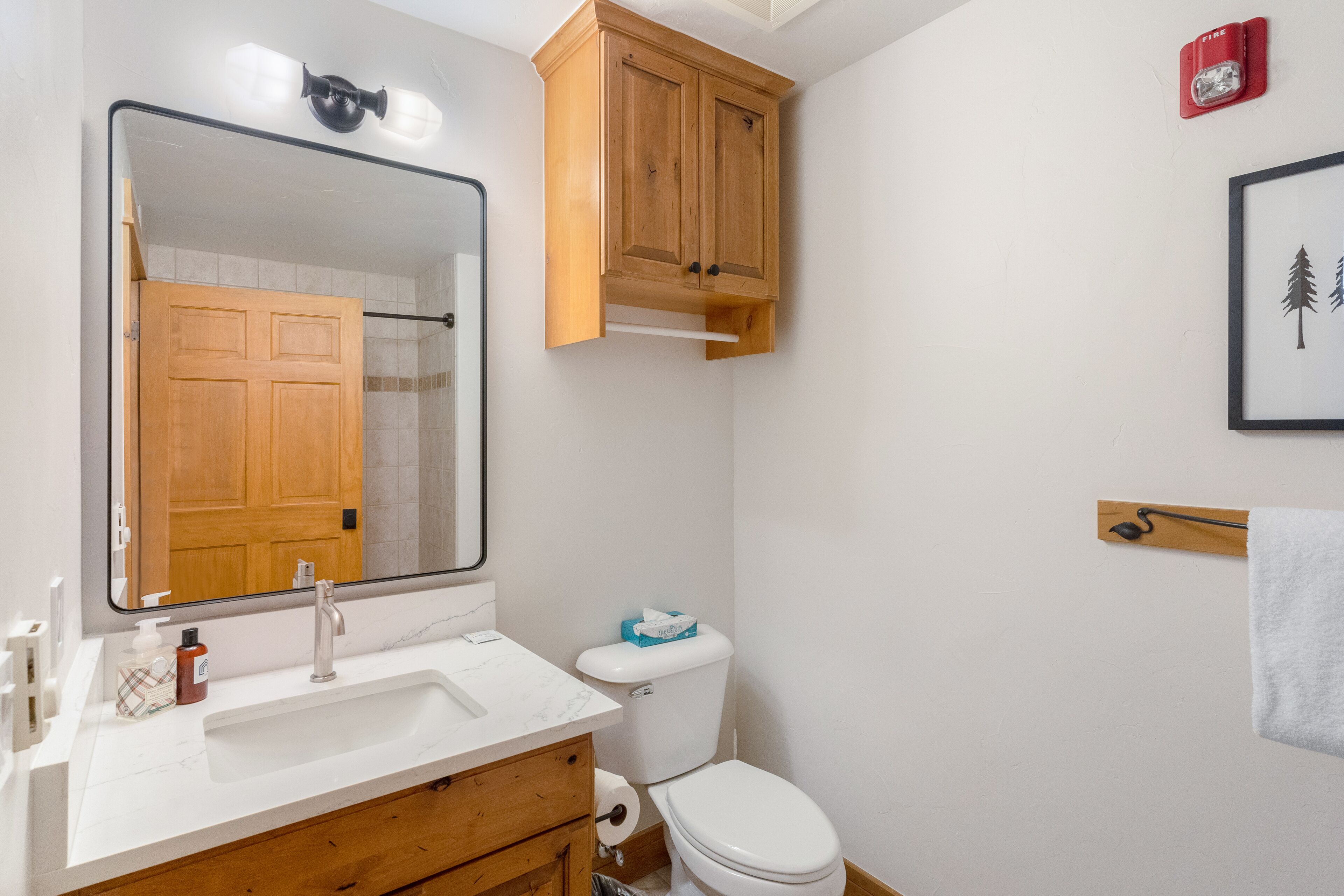 A bathroom with a white sink, wooden cabinet, toilet, and a framed picture on the wall.