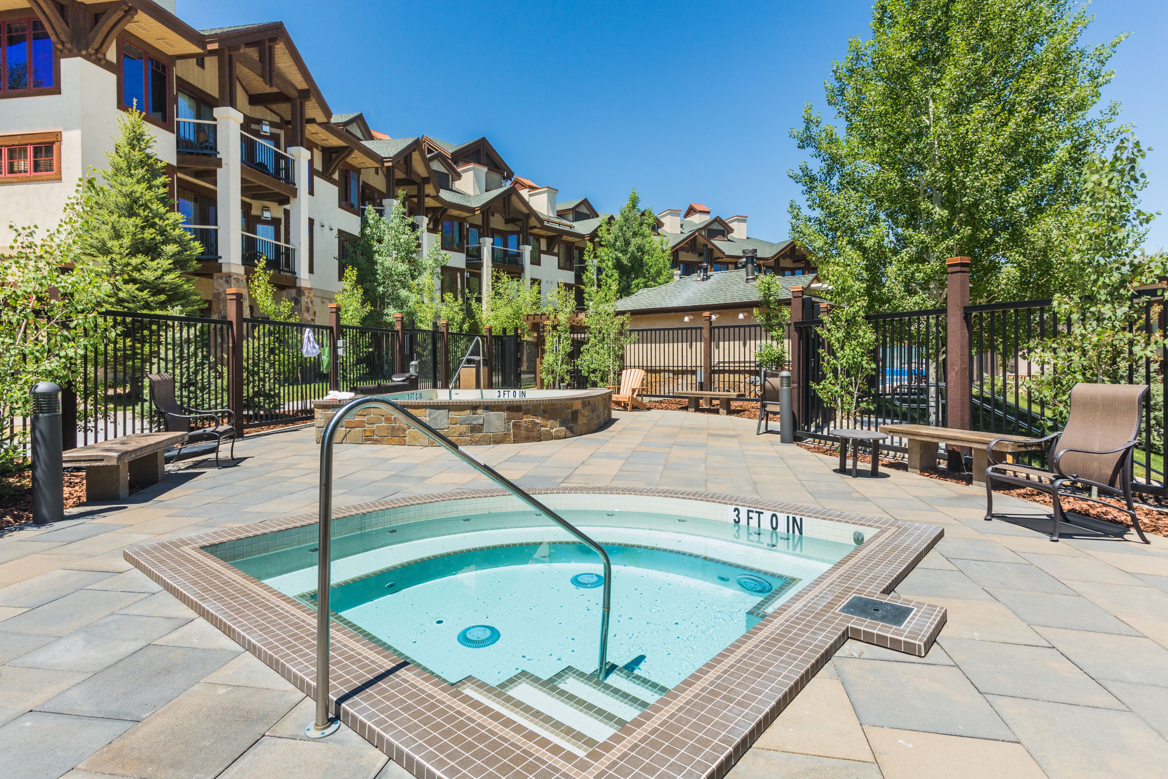 A swimming pool with steps leading into it, surrounded by outdoor seating and a fence.