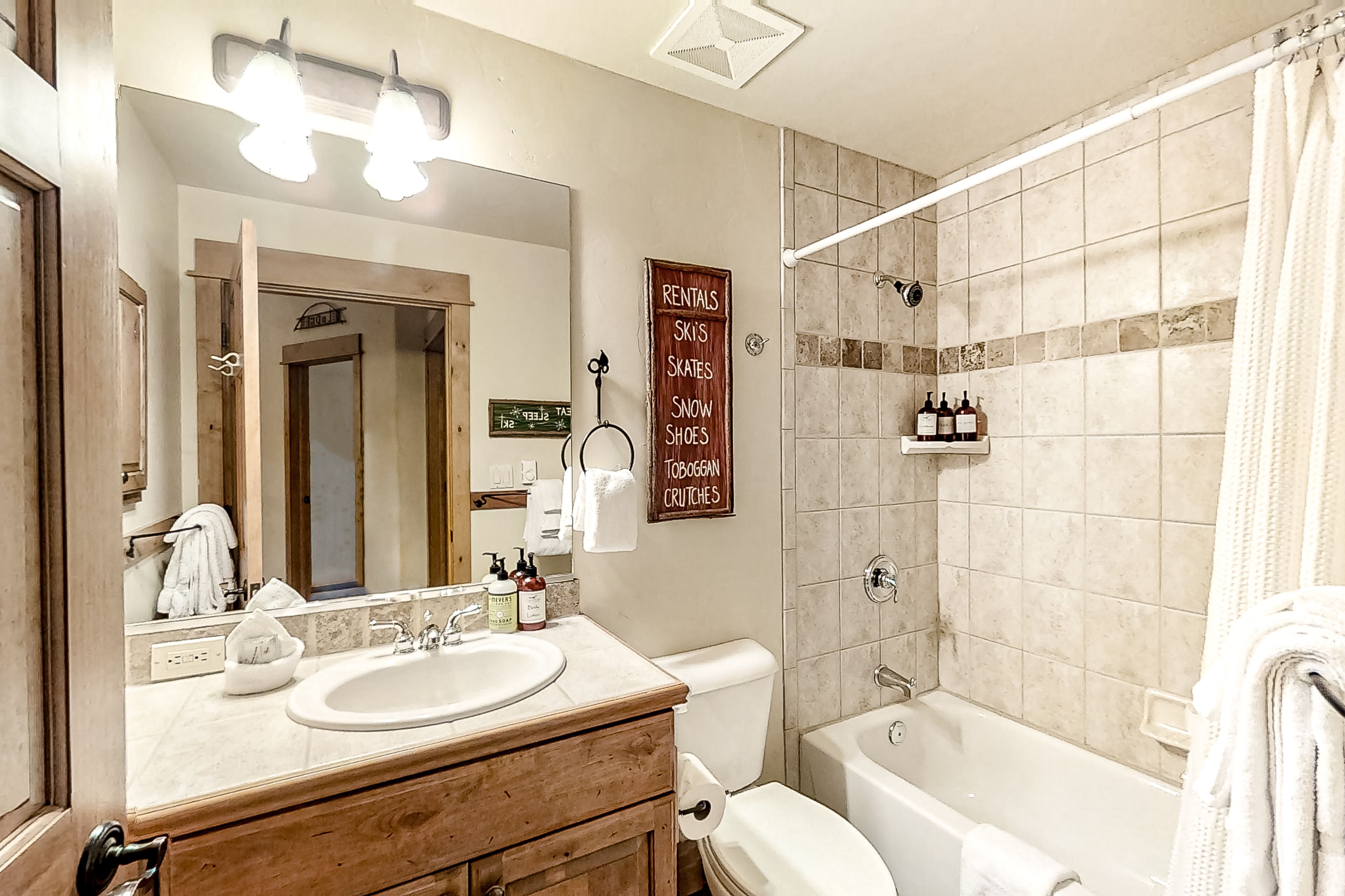A bathroom with a sink, mirror, and a sign listing rentals like skis and snow shoes.