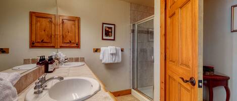 A bathroom with two sinks, a shower, wooden cabinets, and a door.
