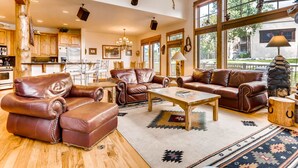 Un salon spacieux, doté de canapés en cuir, d’une table basse en bois et d’une grande fenêtre donnant sur l’extérieur.