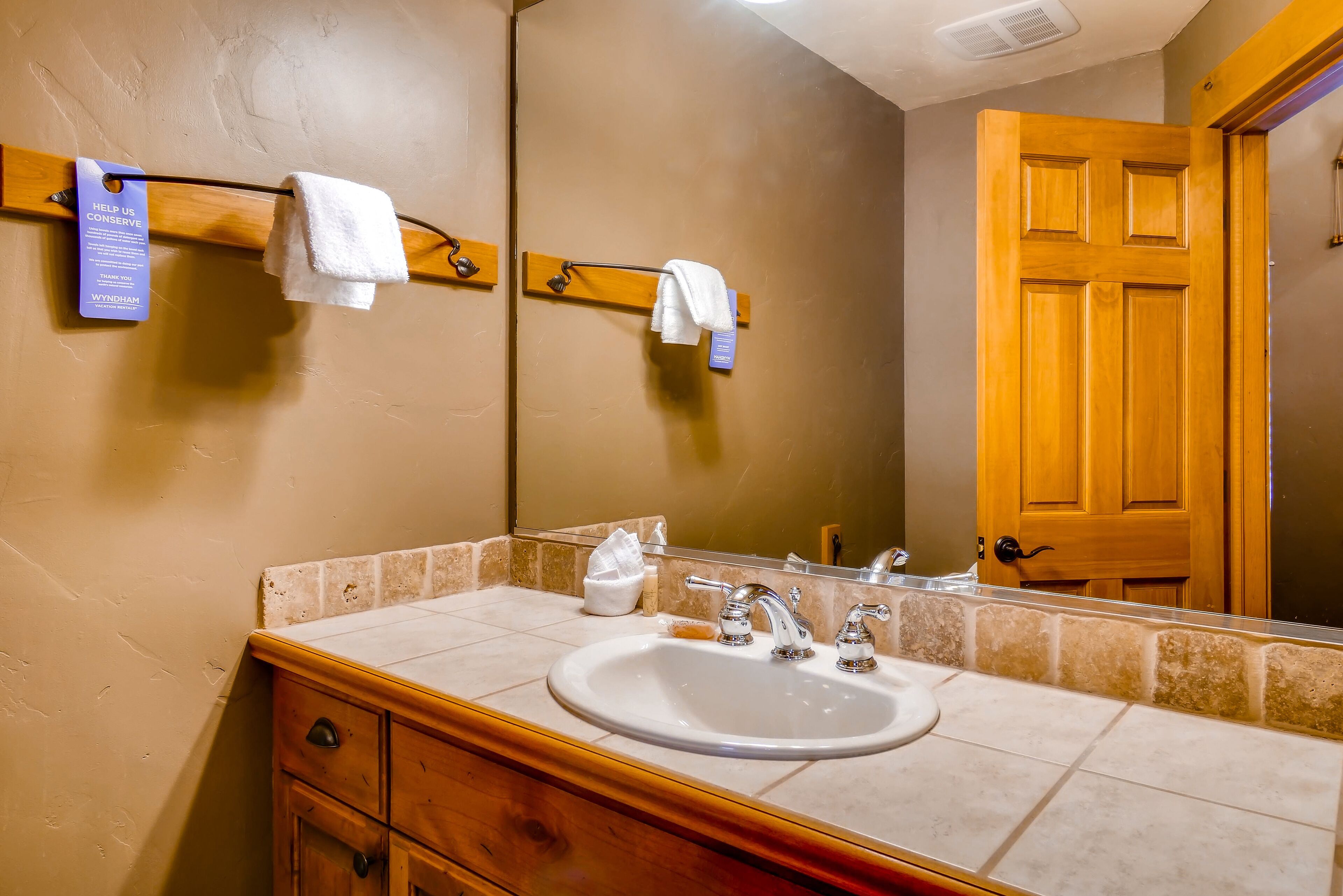 A bathroom with a sink, two towel hooks, a mirror, and a wooden door.
