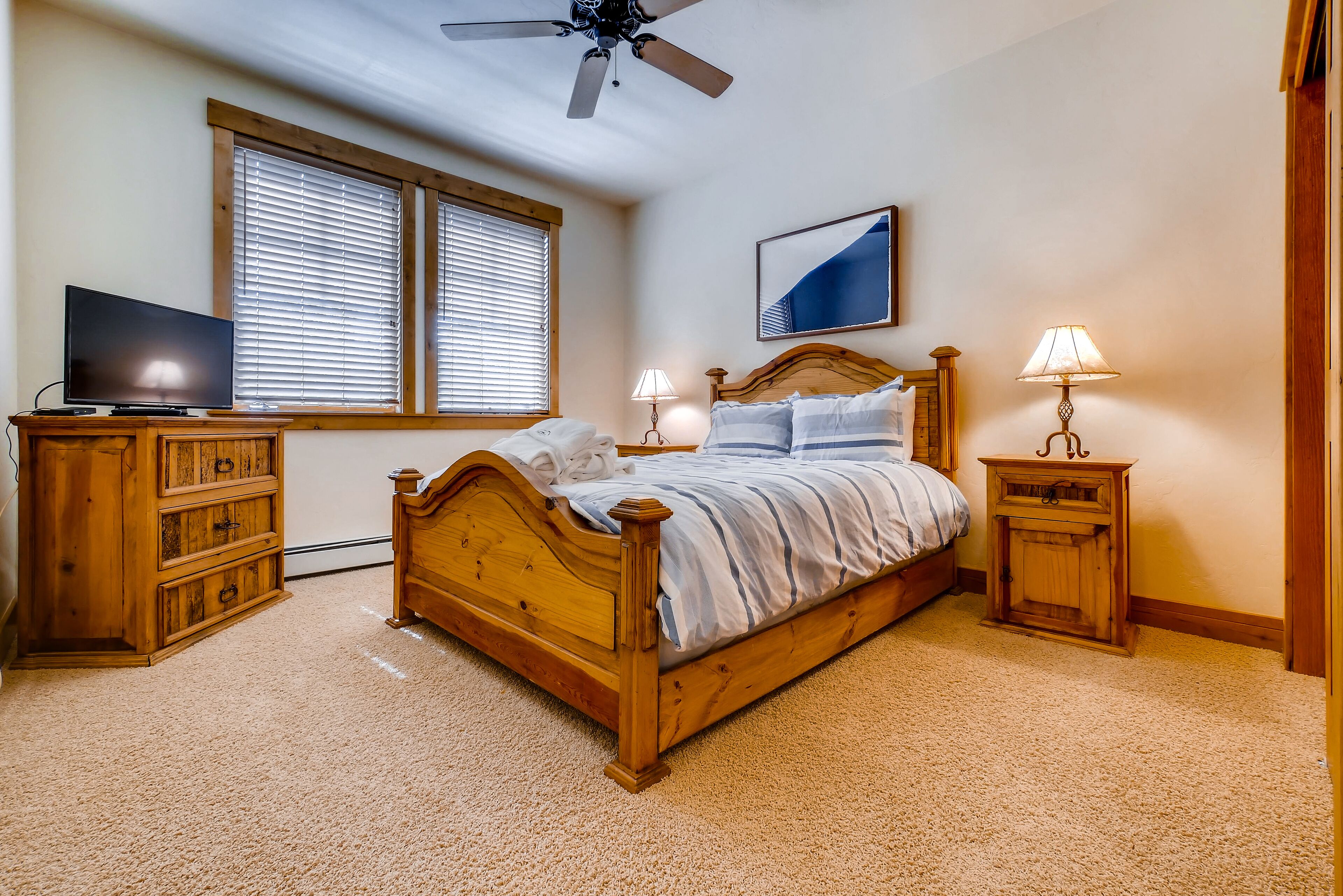 A bedroom with a wooden bed, a television on a wooden dresser, and two bedside lamps.