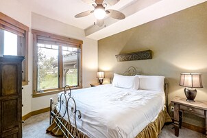 Un dormitorio con cama, dos lámparas de noche, un ventilador de techo y una ventana con vistas al exterior.