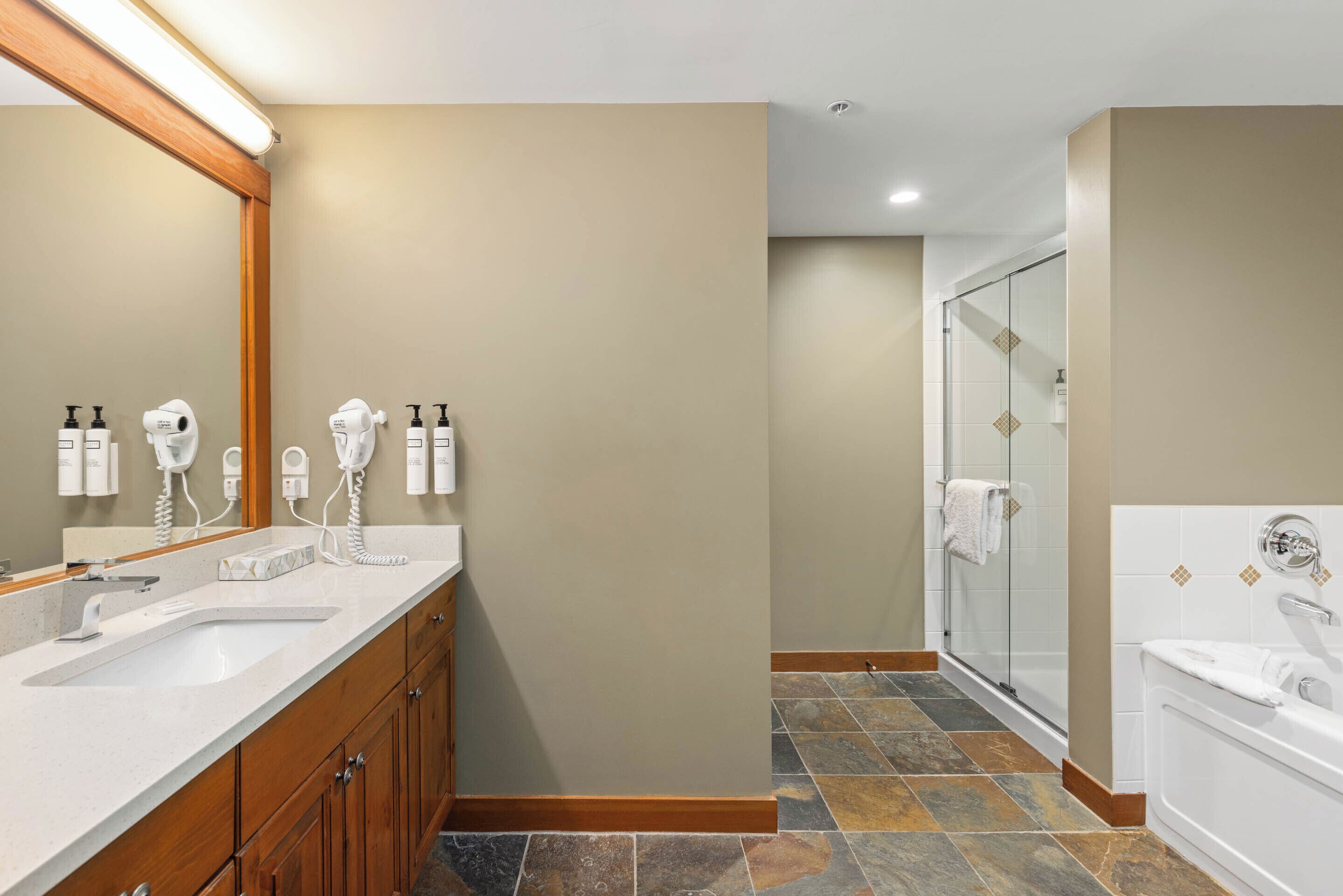 A bathroom with a large mirror, two sinks, a shower, and a bathtub.