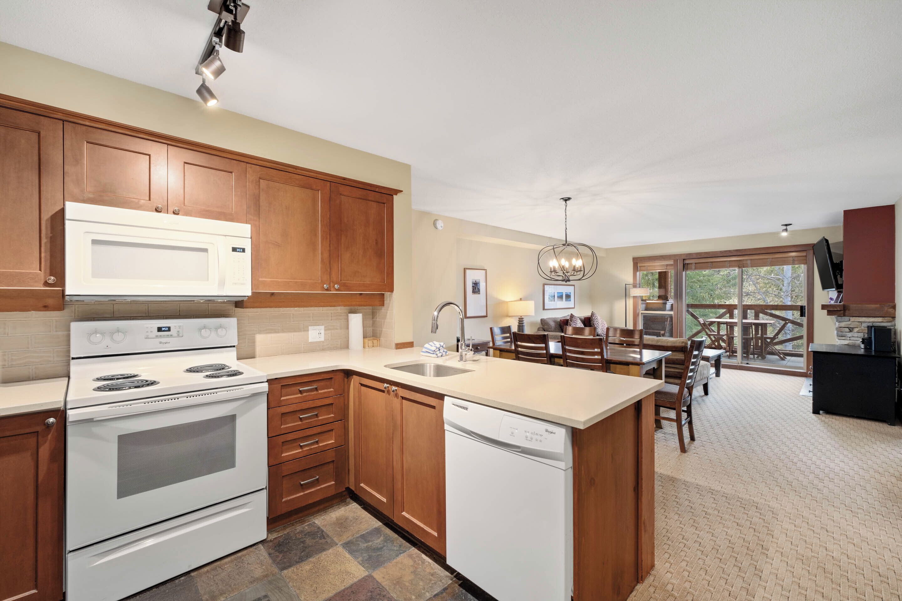 A kitchen with wooden cabinets, a white stove, and a dishwasher. There is a dining area with a table and chairs.