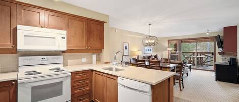 A kitchen with wooden cabinets, a white stove, and a dishwasher. There is a dining area with a table and chairs.