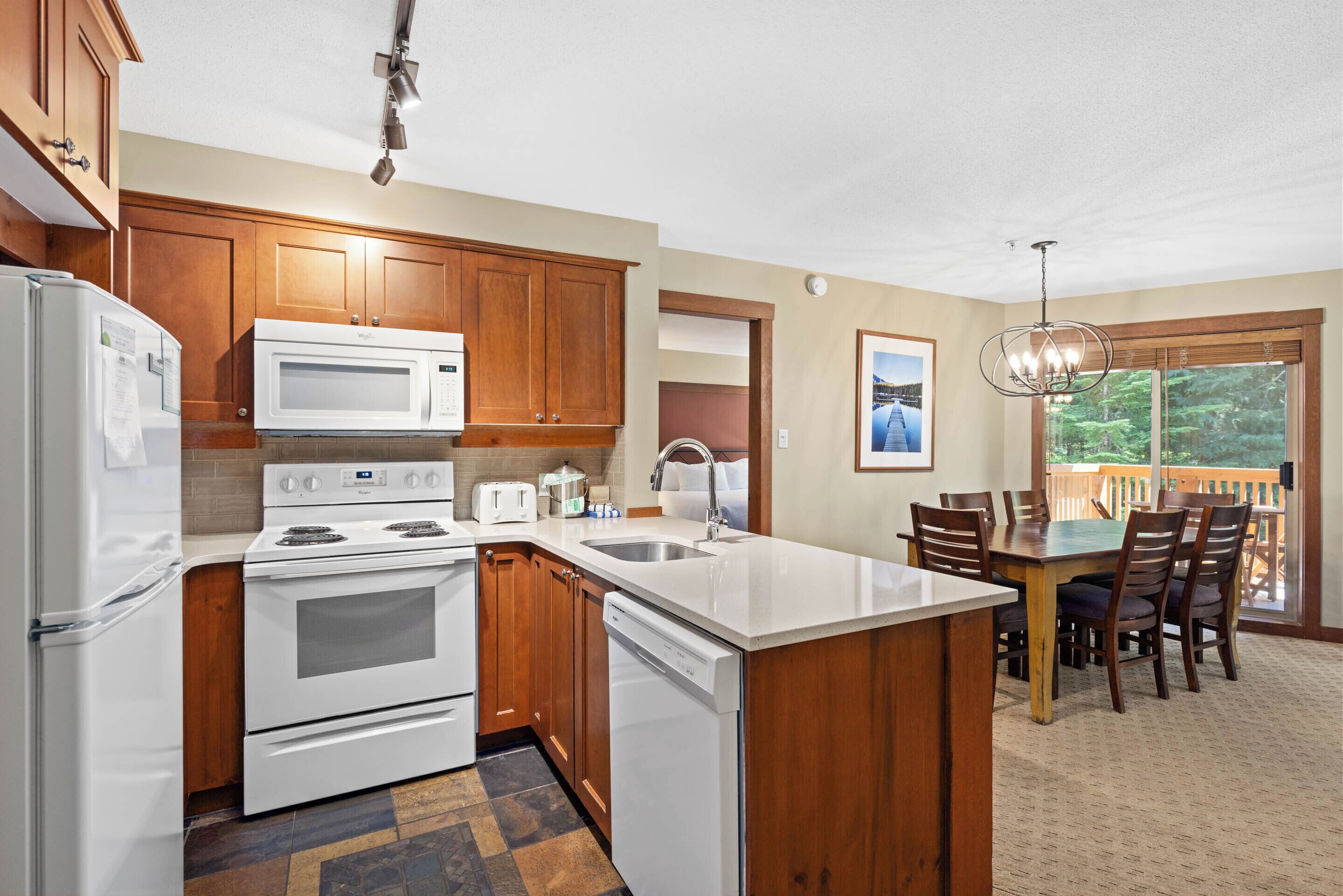 A kitchen with wooden cabinets, a microwave, stove, and dishwasher. There is a dining area with a table and chairs.