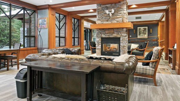 A spacious living area with a stone fireplace, leather seating, and large windows offering a view of the outdoors. - Horstman House by Whistler Premier (Whistler)