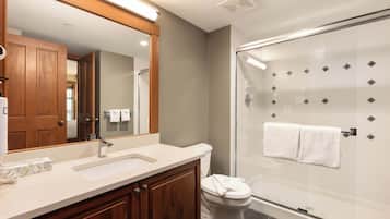 A modern bathroom with a wooden vanity, a large mirror, a glass shower enclosure, and a white toilet.