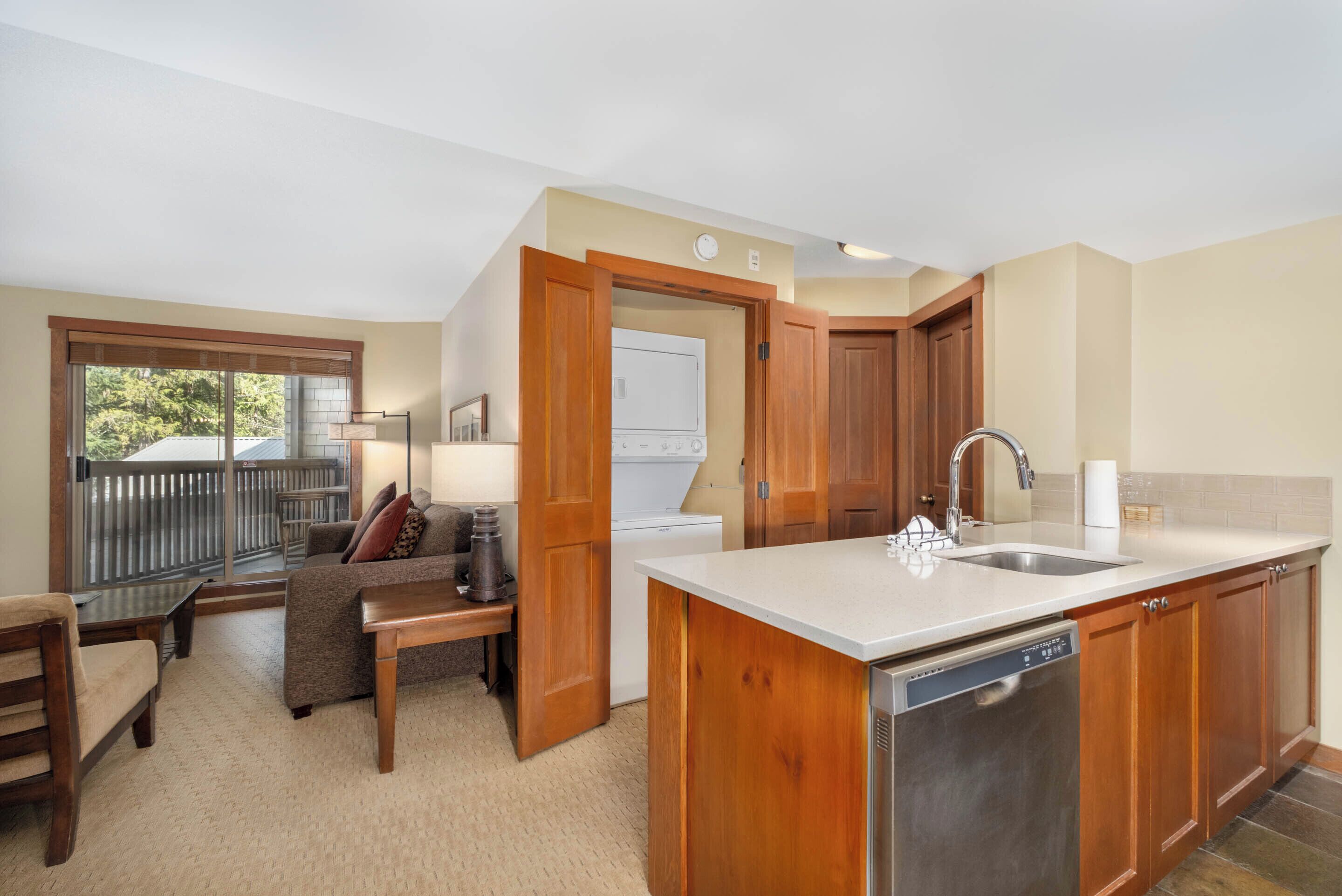 A kitchen with wooden cabinets, a dishwasher, a sink, and a window overlooking a balcony.