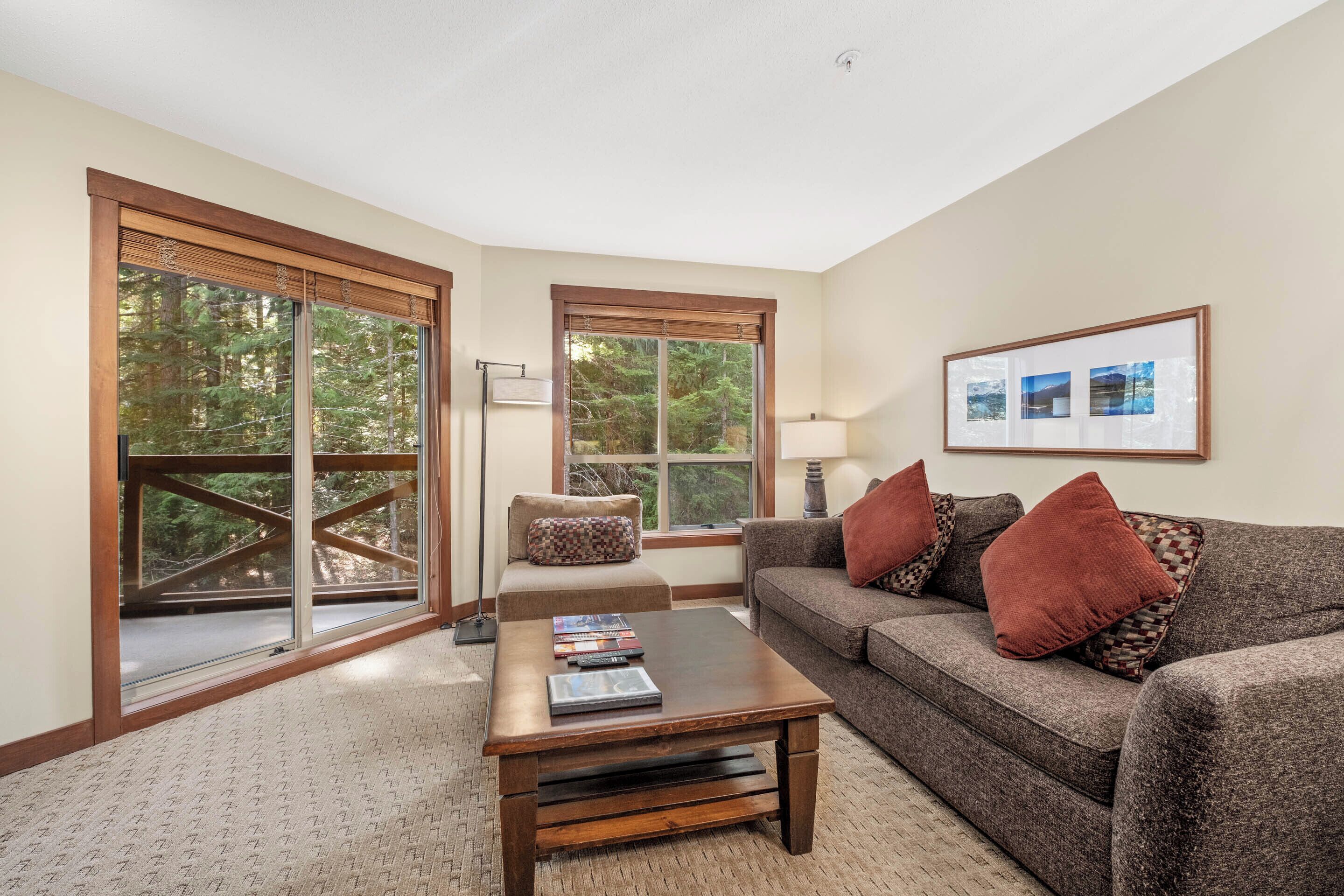 A living room with a sofa, coffee table, and large windows offering a view of trees.