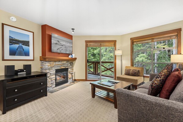 A cozy living room with a fireplace, comfortable seating, and a large window offering a view of the outdoors.