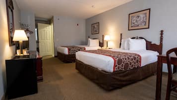 A hotel room with two beds, a desk, a chair, and a door leading to another room.