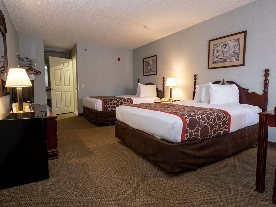 A hotel room with two beds, a desk, a chair, and a door leading to another room.