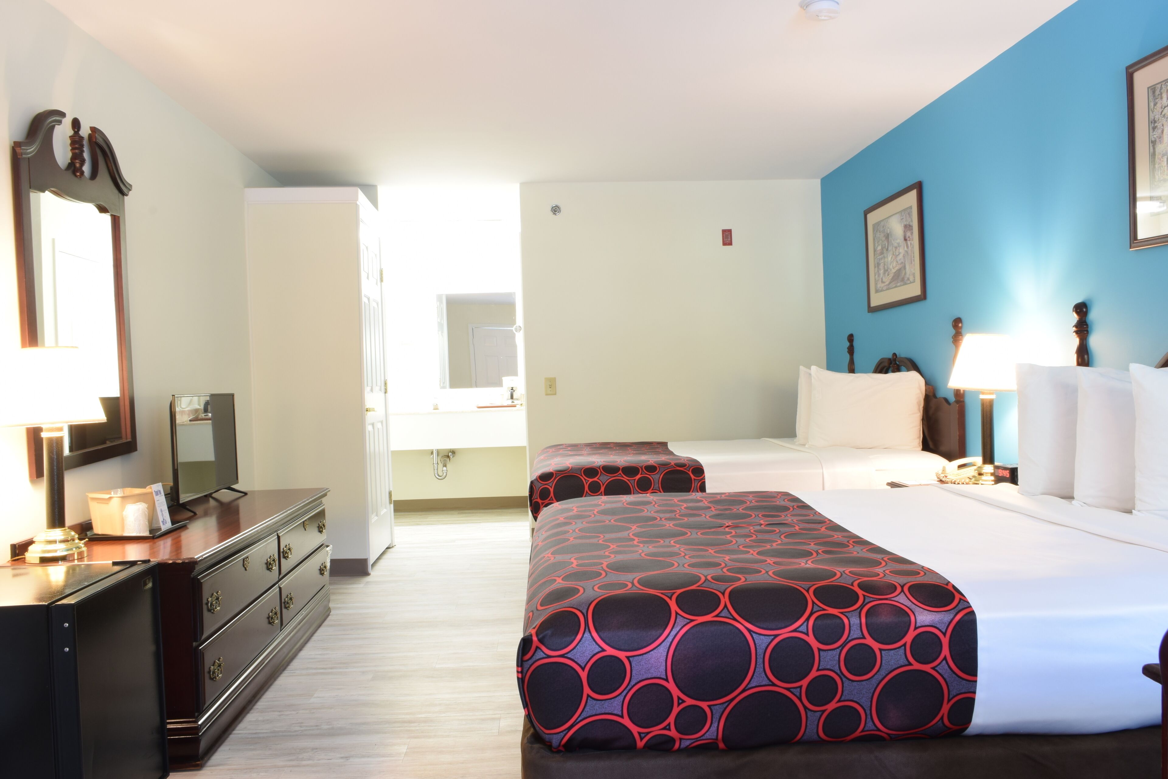 A hotel room with a bed, bedside table, lamp, dresser, and a mirror.