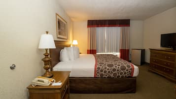 Une chambre d’hôtel comprenant un lit, des lampes de chevet, une commode, un téléviseur et un bureau avec un téléphone et des documents.