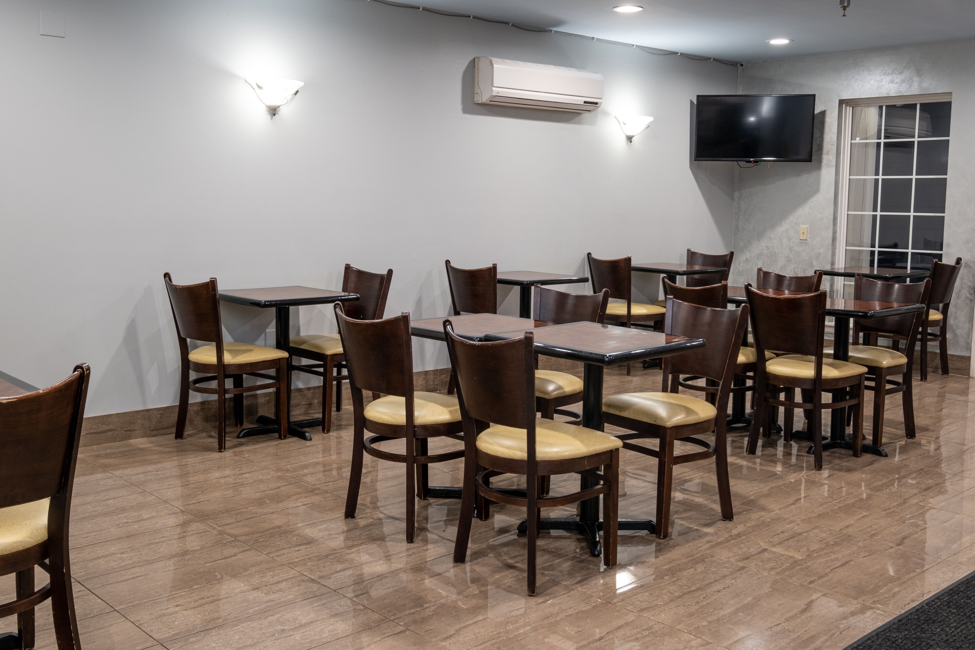 A dining area with multiple tables and chairs, an air conditioning unit, a television, and a window with blinds.