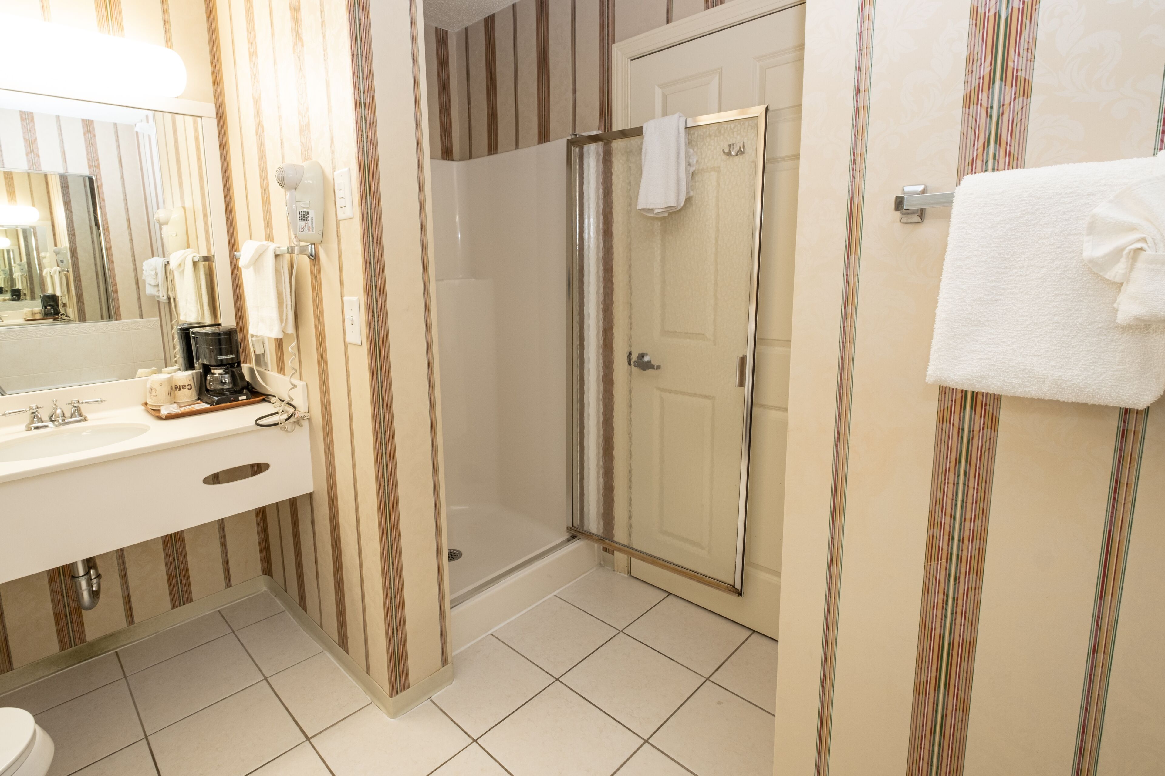 A bathroom with a shower, a sink with a coffee maker, and a mirror.