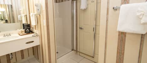 Un baño con ducha, lavabo y cafetera, y un espejo.