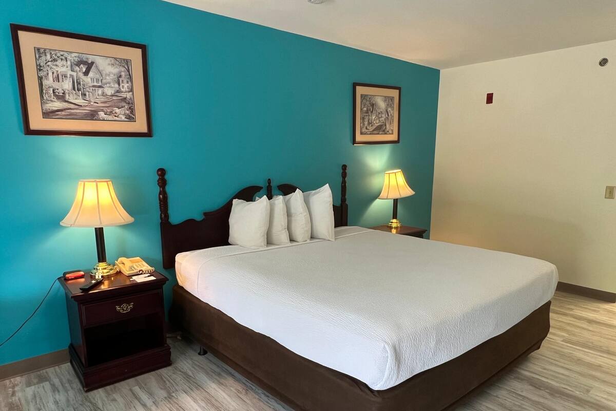 Una cama cuidadosamente tendida en una habitación con paredes color turquesa, dos mesitas de noche con lámparas y cuadros enmarcados en las paredes.