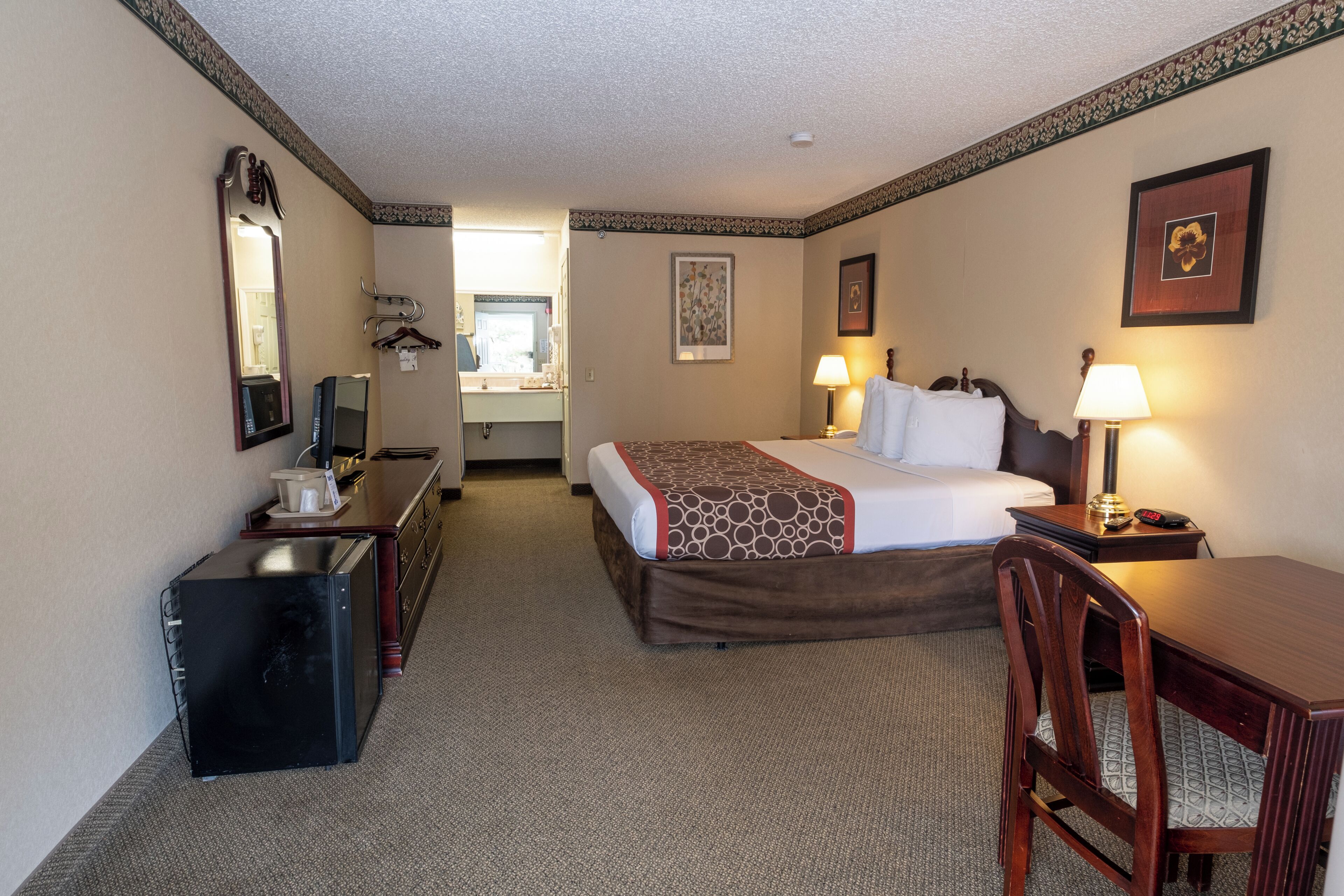 A hotel room with a bed, desk, chair, and a mirror.