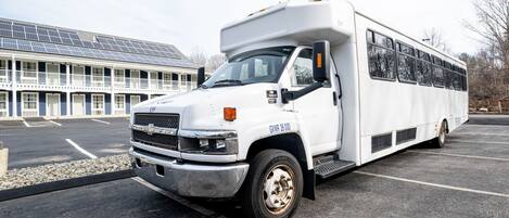 A white RV parked in a lot with a building featuring solar panels in the background.