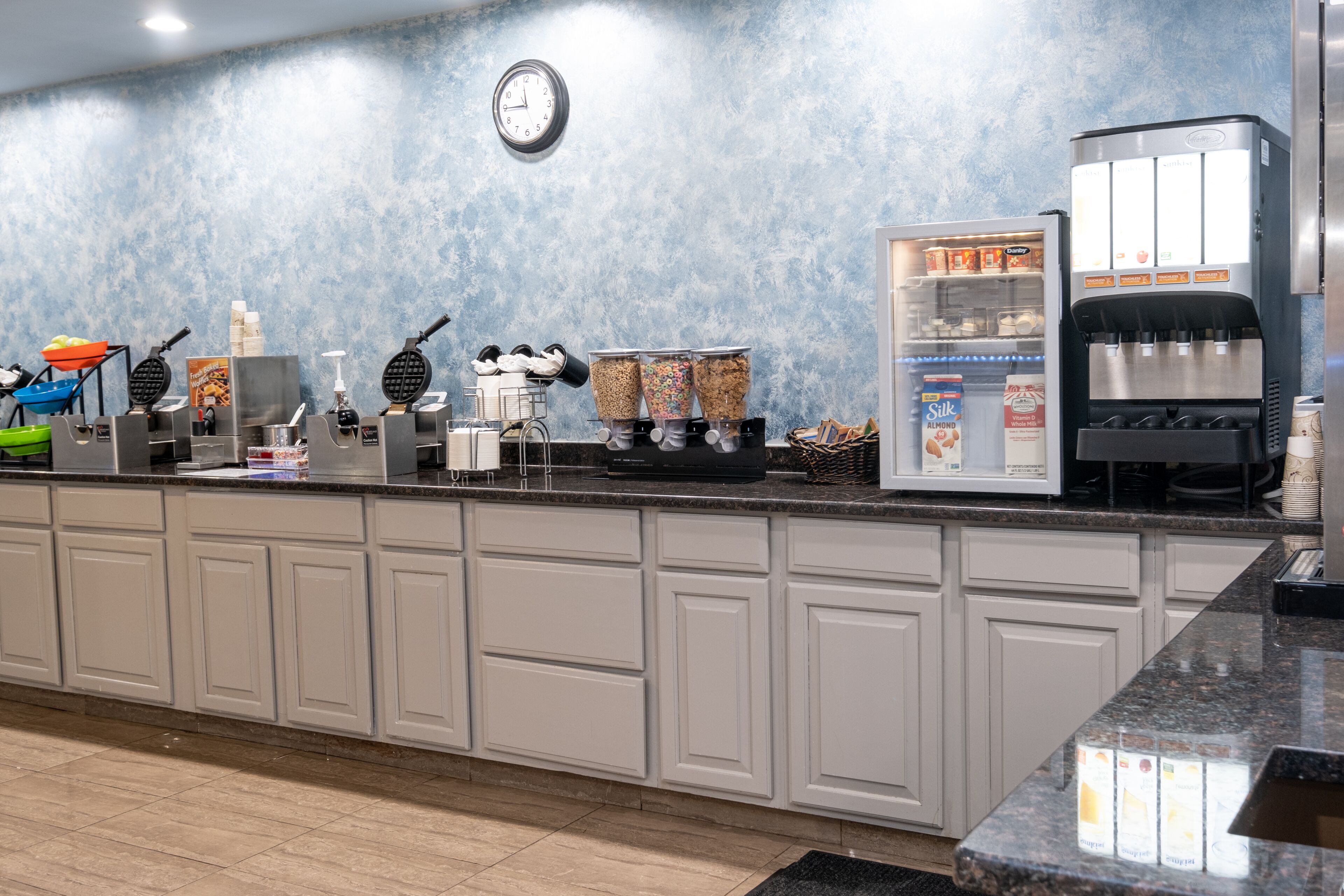 Een ontbijtbuffet met wafelapparaten, een koffieapparaat en een gekoelde display met melkverpakkingen.