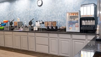 Een ontbijtbuffet met wafelapparaten, een koffieapparaat en een gekoelde display met melkverpakkingen.