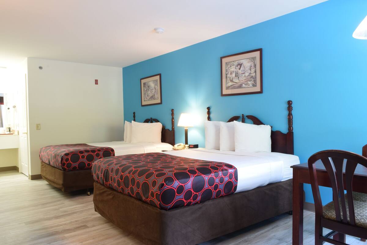 Habitación de hotel con dos camas, un cabecero de madera, una mesita de noche con lámpara y dos cuadros enmarcados en la pared.