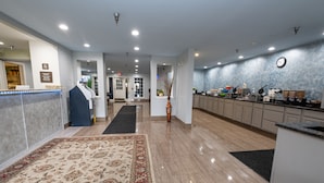 Um saguão de hotel com uma mesa de recepção, uma área de cozinha e um corredor que dá acesso a outros quartos.
