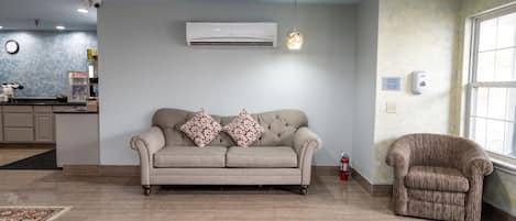 Una sala de estar con un sofá color beige, un sillón estampado y una alfombra.