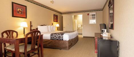 A hotel room with a bed, a desk, a chair, a coffee maker, and a door leading to a bathroom.