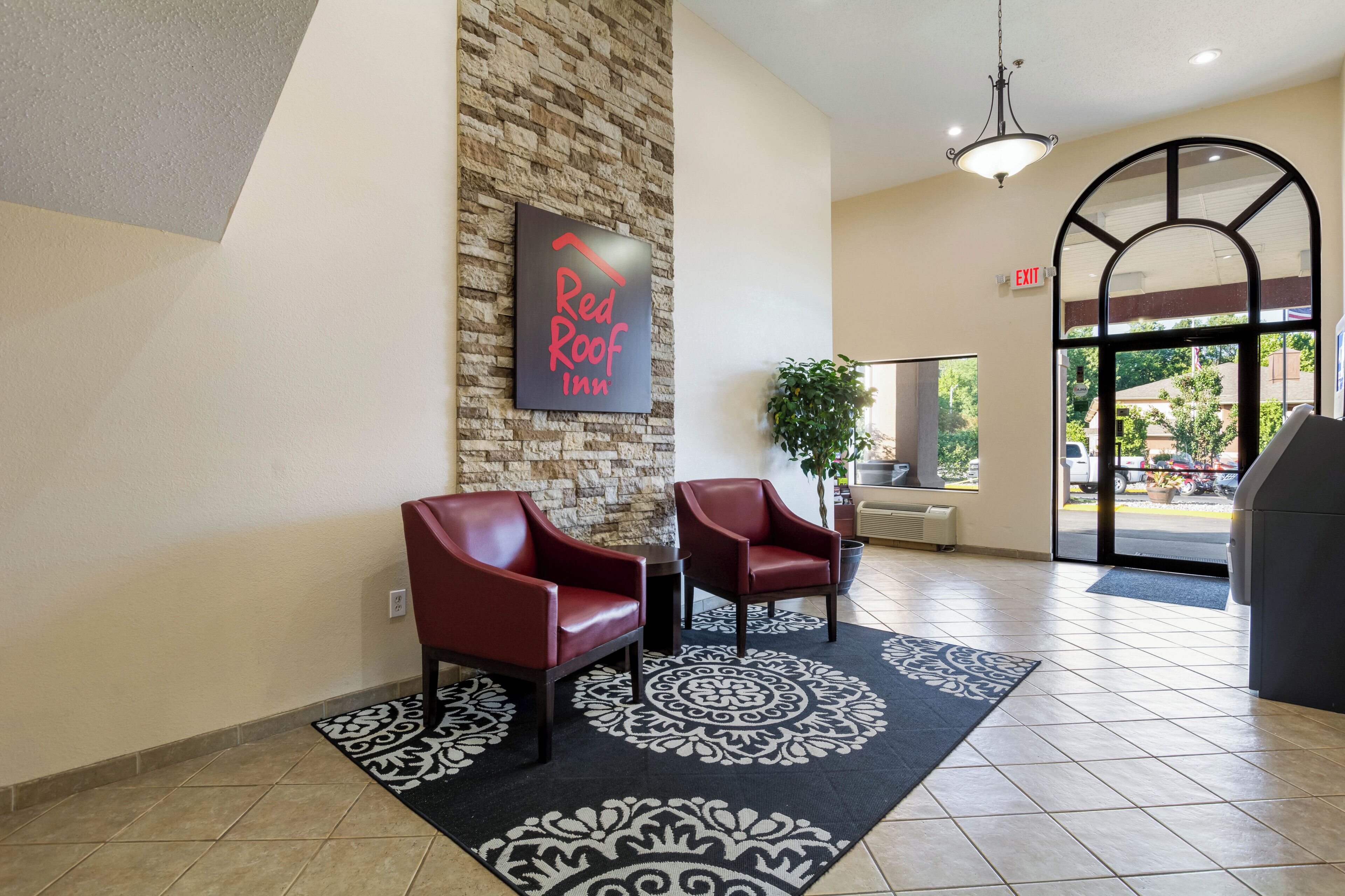 A Red Roof Inn reception area with two leather chairs, a wall-mounted sign, a potted plant, and a patterned rug.