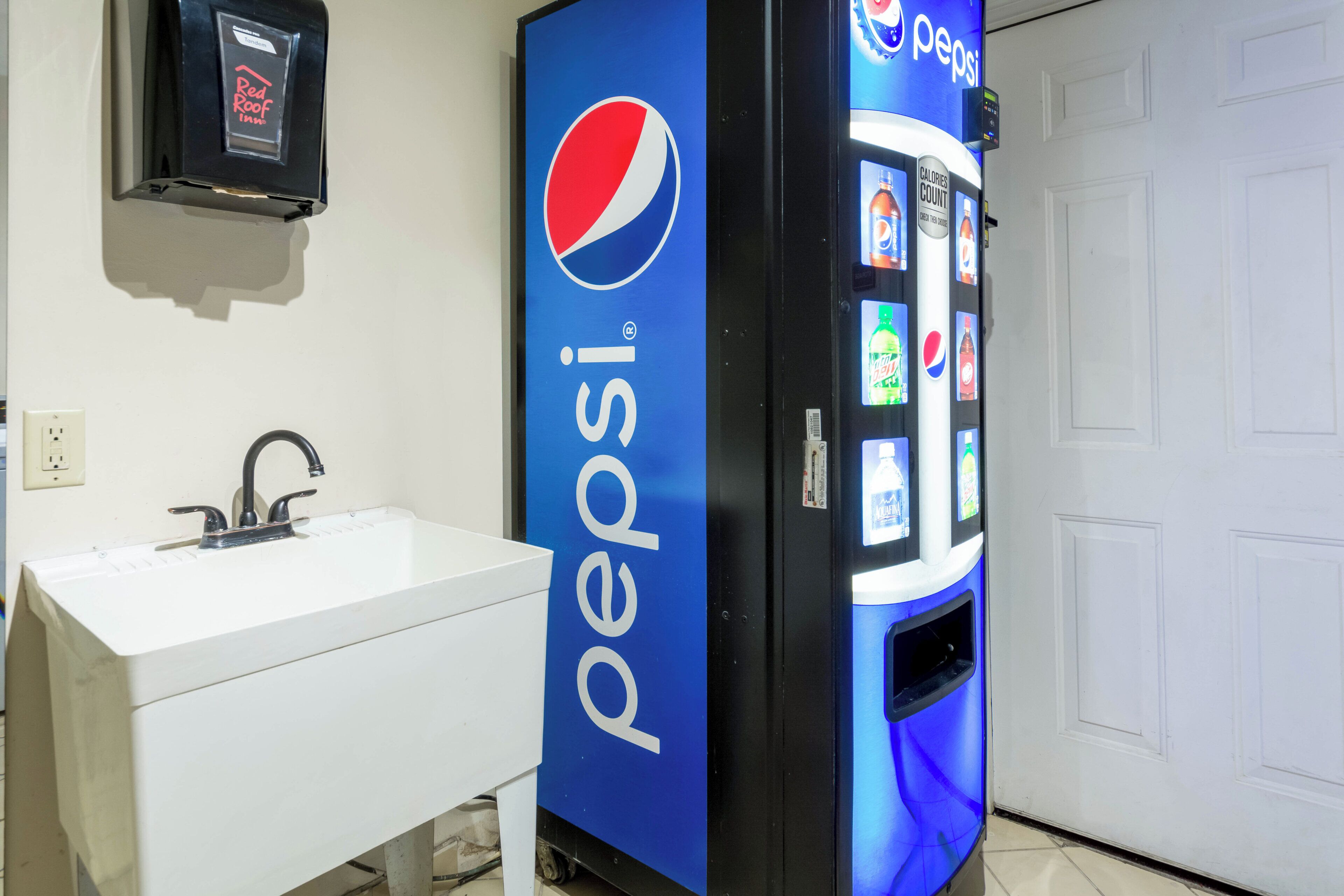 A bathroom with a white sink, a black faucet, and a blue Pepsi vending machine.