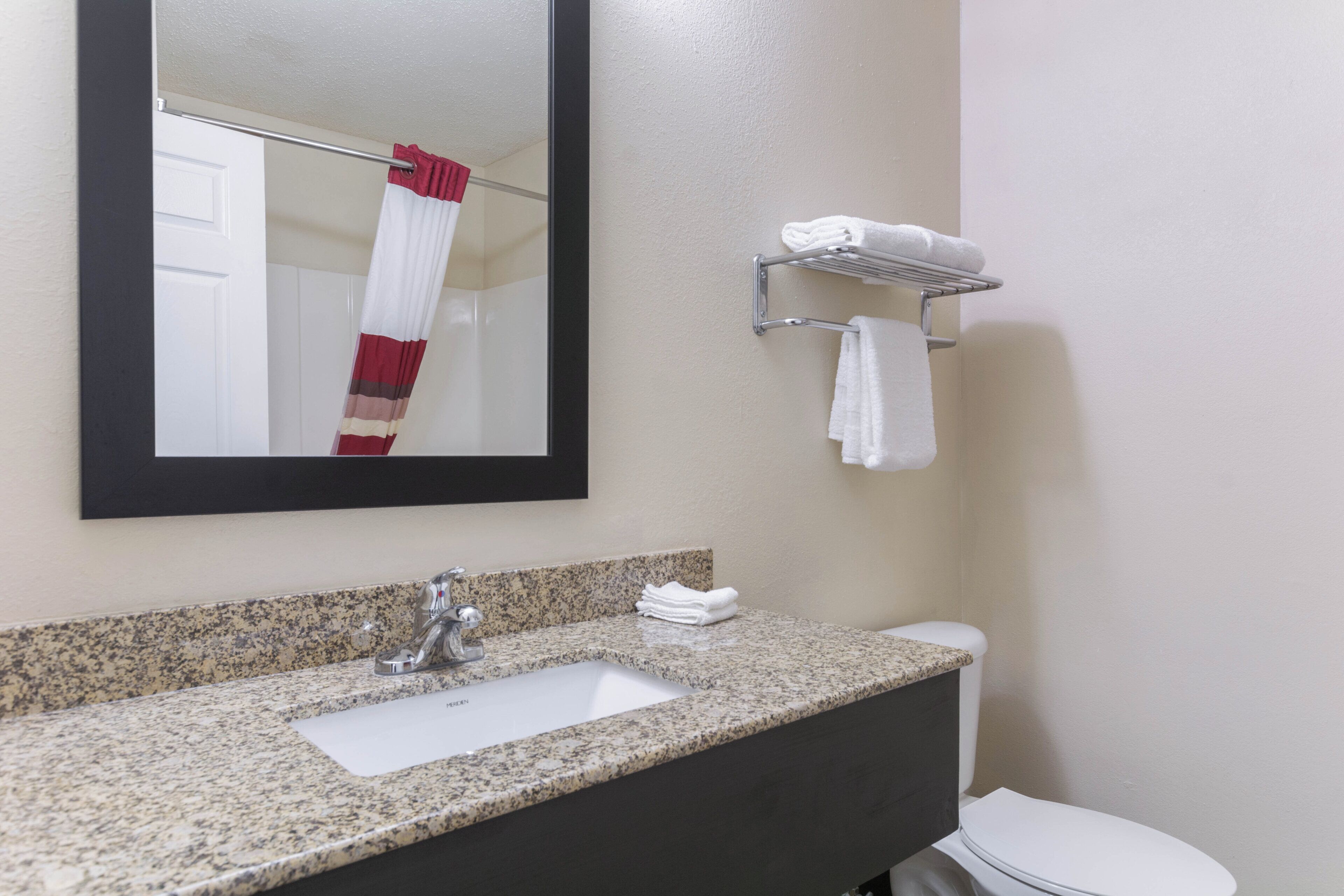 A bathroom with a granite countertop sink, a mirror, a towel rack, and a toilet.
