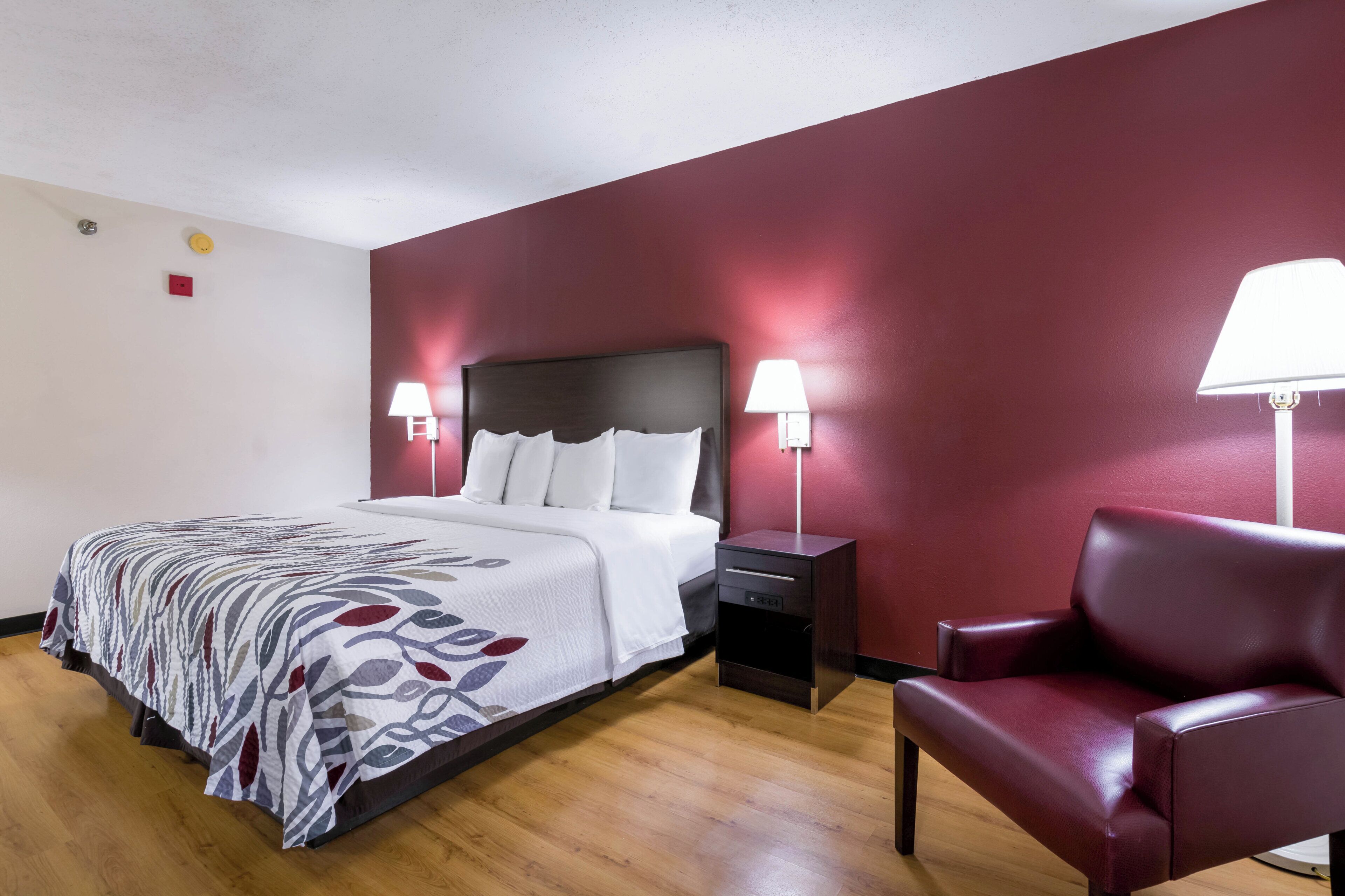 A hotel room with a bed, bedside lamps, a chair, and a nightstand.