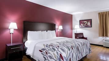 A hotel room with a large bed, two bedside tables, a chair, a desk, and a picture on the wall.