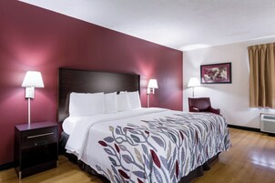 Una habitación de hotel con una cama grande, dos mesitas de noche, una silla, un escritorio y un cuadro en la pared.