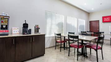 Un área de cocina limpia y moderna con cafetera, máquina para hacer gofres y microondas. Hay varias sillas y una mesa, lo que sugiere un comedor.