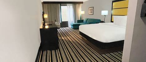 A hotel room with a large bed, a desk, a chair, a sofa, and a window with curtains.