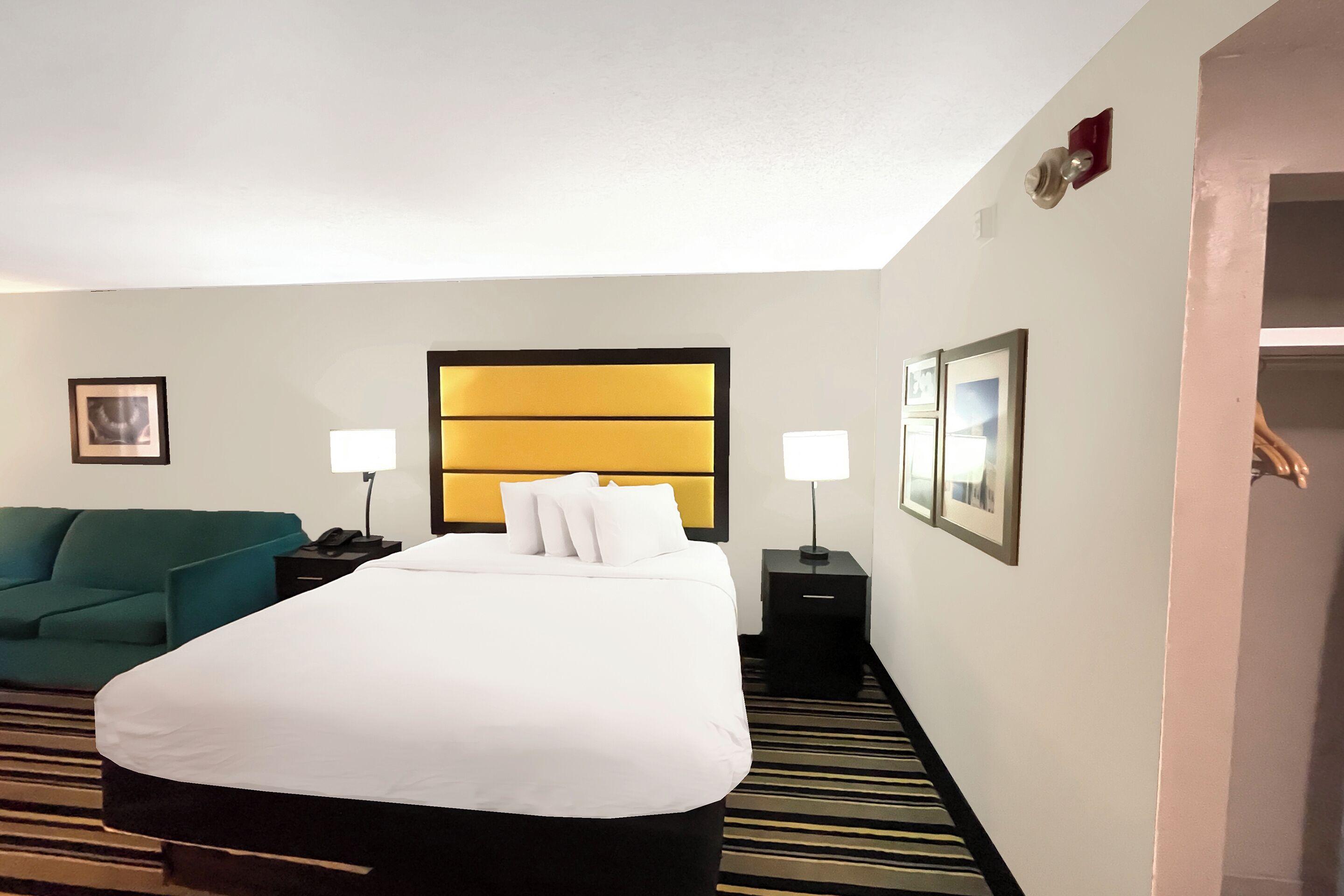 A hotel room with a large bed, two bedside tables, a green sofa, and a striped carpet.
