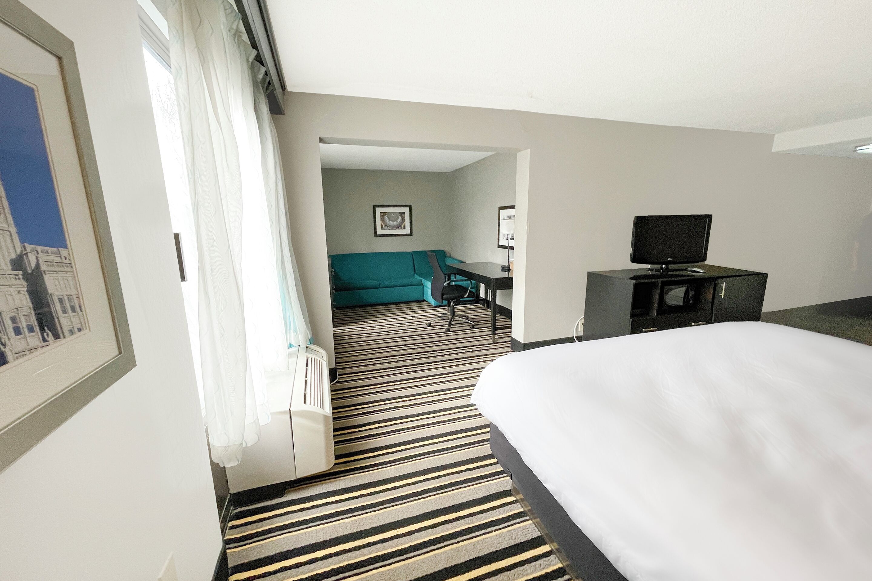 Et hotelværelse med seng, skrivebord, fjernsyn, stol og sofa.
