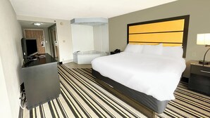 Habitación de hotel con una cama grande, televisión de pantalla plana, escritorio, silla, espejo y baño con bañera y ducha.