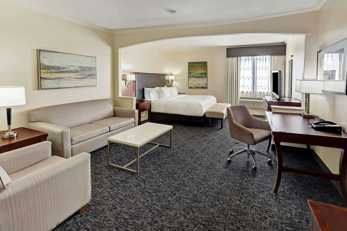 A hotel room with a bed, a sofa, a desk, a chair, a coffee table, and artwork on the walls.