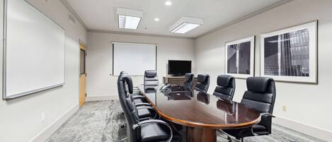 A conference room with a large oval table, black leather chairs, a whiteboard, and framed pictures on the wall.